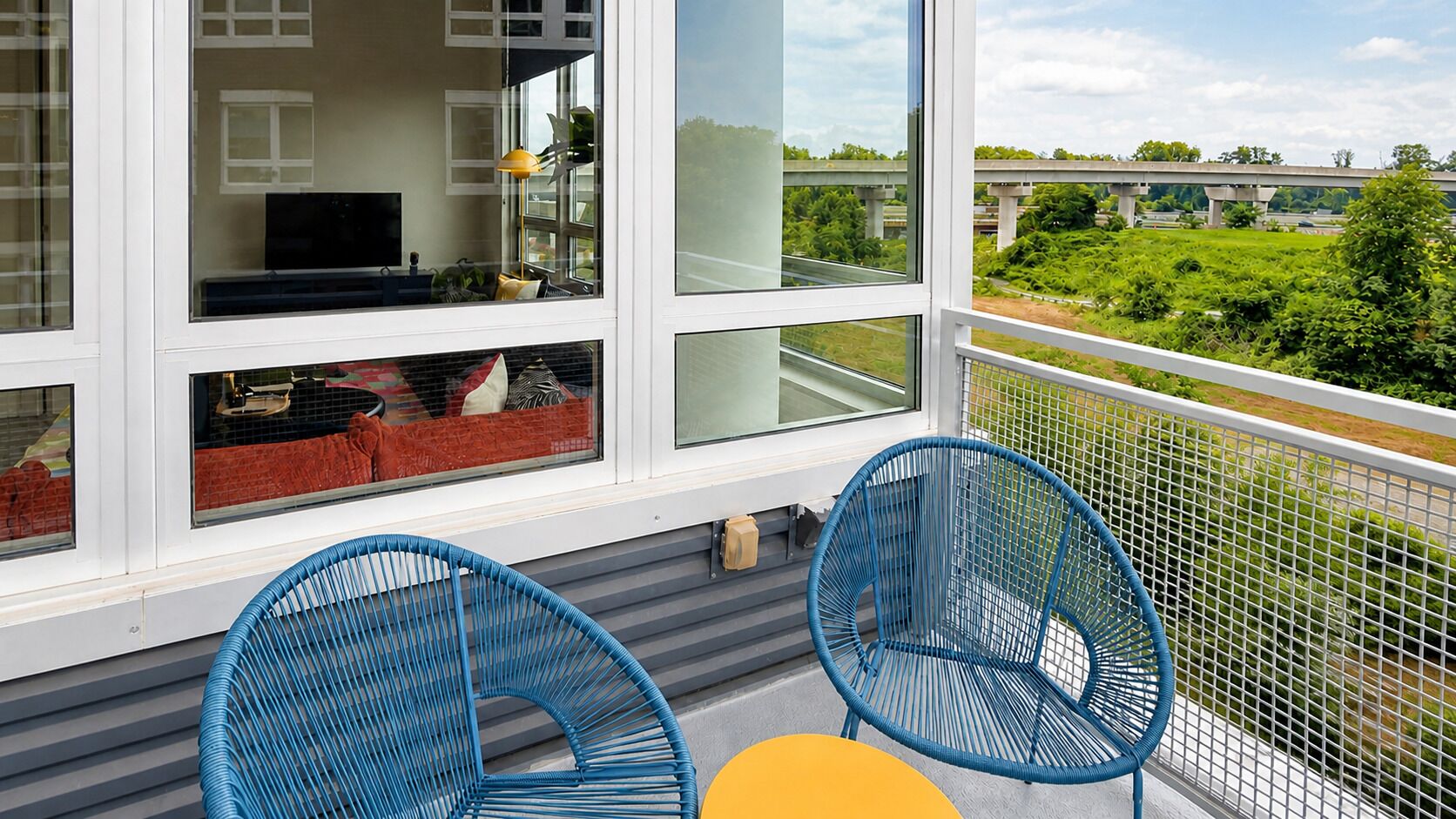 Ein Balkon mit zwei blauen Stühlen und einem gelben Tisch.