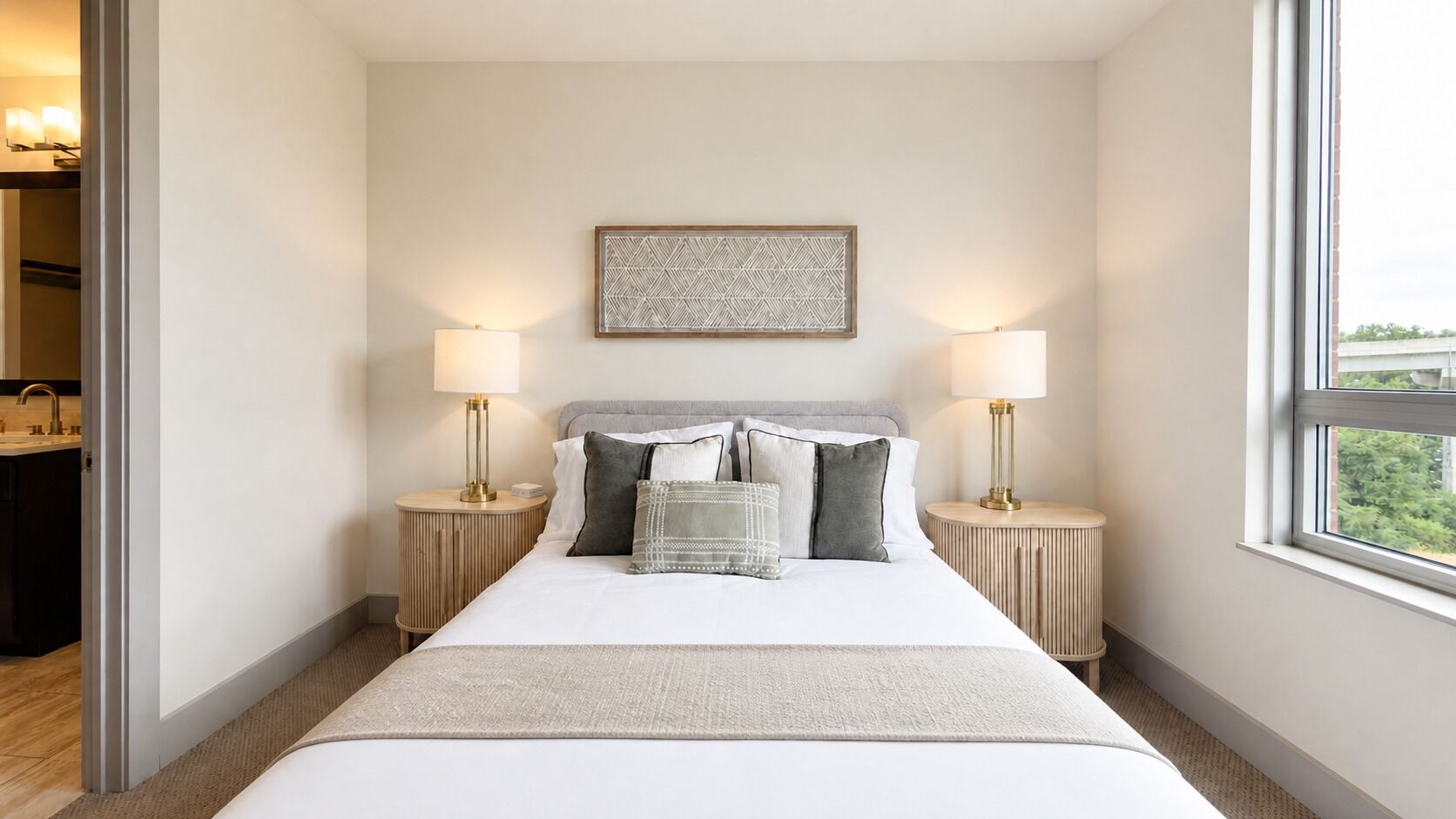 A hotel room with a large bed, two bedside tables, a wall-mounted artwork, and a window with a view.