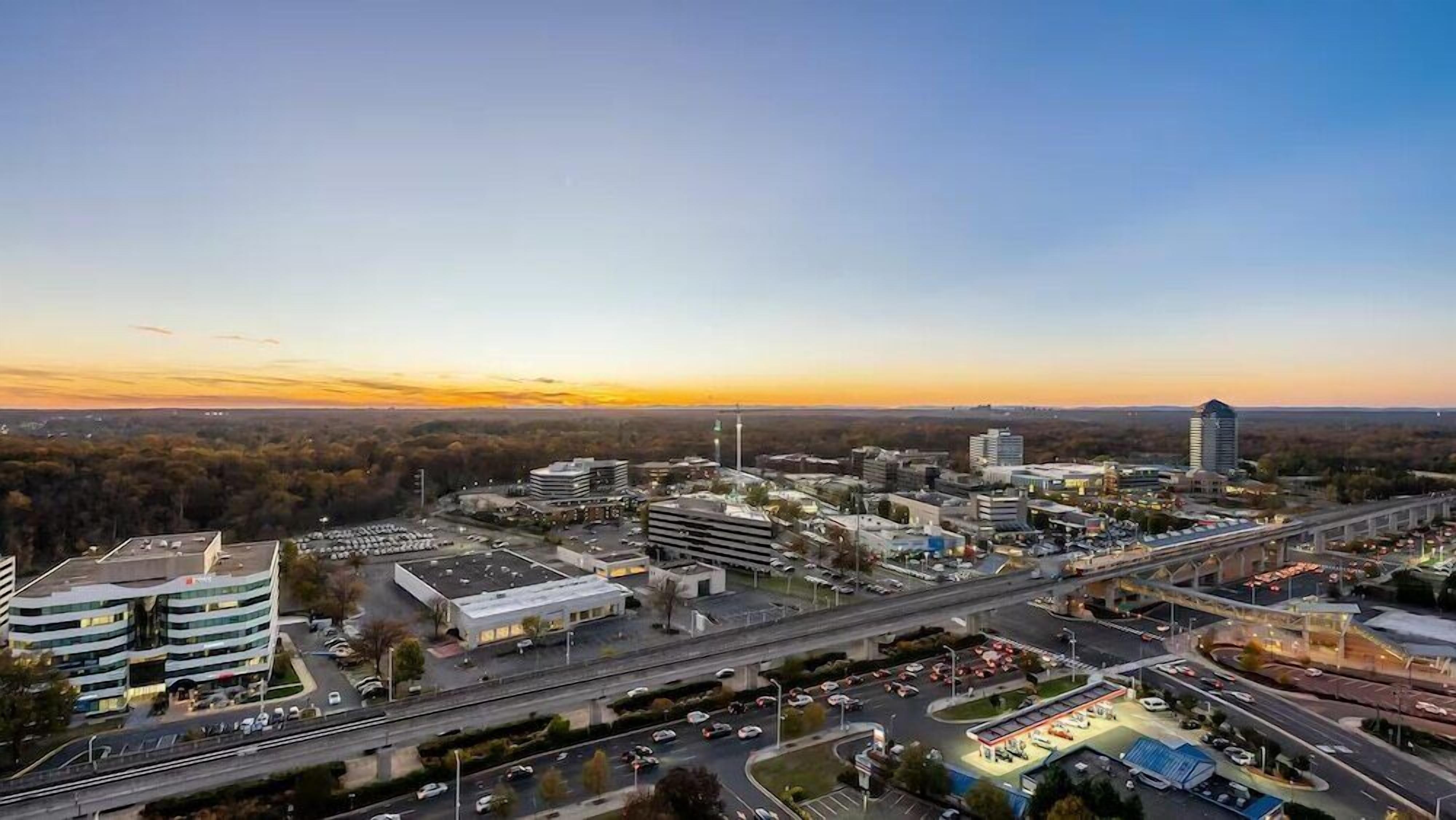 An aerial view of a cityscape with modern buildings, roads, and a highway interchange.
