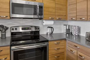 A kitchen with stainless steel appliances, wooden cabinets, and a marble countertop.