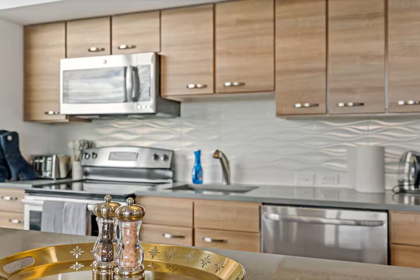 A modern kitchen with wooden cabinets, stainless steel appliances, and a decorative salt and pepper set on a tray.