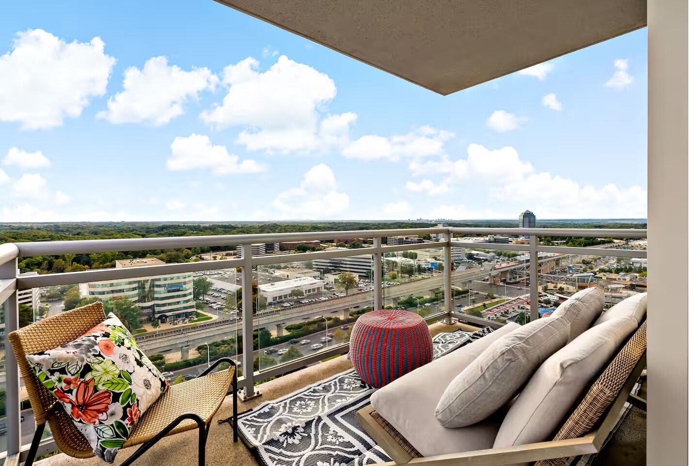 A balcony with a sofa, a wicker chair, and a patterned rug.