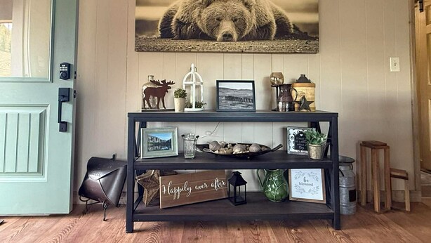 A room with a wooden console table displaying various items, a mounted picture of a bear, and a door with a light blue frame.