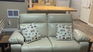 Una sala de estar con sofá de cuero, alfombra de piel de vaca, una zona de cocina con mesa de madera e iluminación colgante.