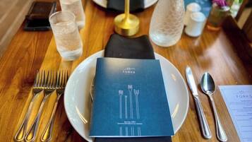 A neatly set dining table with a menu, glasses of water, cutlery, and a decorative bottle.