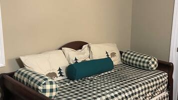 A small, cozy room with a checkered bedspread, a wooden headboard, and a single teal pillow.