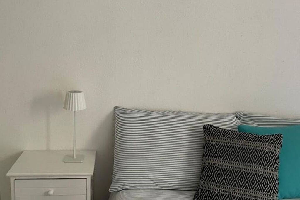 A neatly arranged bedroom with a single bed, a bedside table with a lamp, and a small drawer.