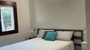 Ein Schlafzimmer mit Bett, Fenster, Nachttisch und Wandleuchte.