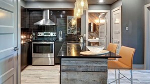 A modern kitchen with stainless steel appliances, a wooden island, and a hanging light fixture. - 120 Algonquin Unit 7 (Mont-Tremblant)