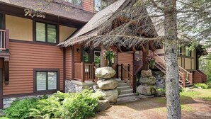 A two-story building with a wooden exterior, a stone staircase, and a thatched roof porch. - 120 Algonquin Unit 7 (Mont-Tremblant)