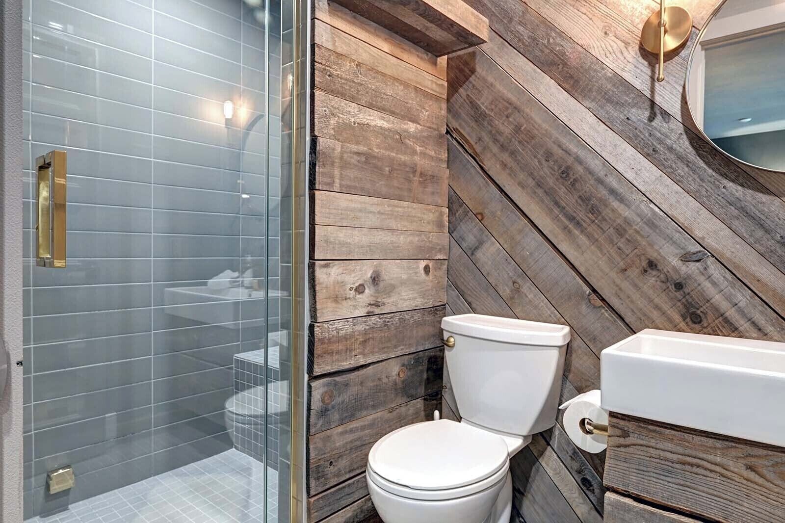 A bathroom with a glass shower enclosure, a white toilet, and a wooden wall design.