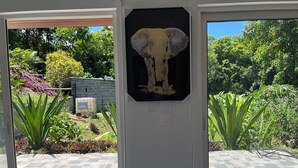 A room with a view of a garden, a door with a framed picture of an elephant, and a tiled floor. - Stay in Guadeloupe : 5 minutes: beaches, downtown Le Moule by car (Le Moule)