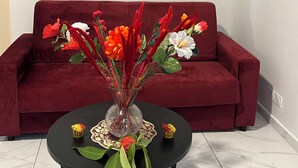 A room with a red sofa, a round table with a vase of flowers, and a painting on the wall. - Stay in Guadeloupe : 5 minutes: beaches, downtown Le Moule by car (Le Moule)