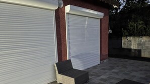 A covered outdoor seating area with two wicker chairs and a table, adjacent to a building with two large garage doors. - Stay in Guadeloupe : 5 minutes: beaches, downtown Le Moule by car (Le Moule)
