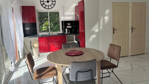 A modern kitchen with red cabinets, a black countertop, and a window with greenery outside. - Stay in Guadeloupe : 5 minutes: beaches, downtown Le Moule by car (Le Moule)