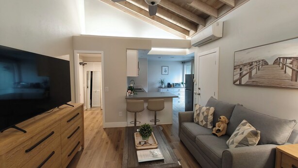 Un soggiorno moderno con televisione a schermo piatto, mobili in legno, un divano grigio con cuscini decorati e un tavolino con oggetti ornamentali.