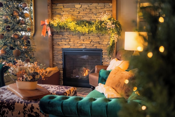 A cozy living room with a fireplace, a Christmas tree, and a green armchair.