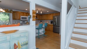 A spacious kitchen with wooden cabinets, a central island with bar stools, and a stainless steel refrigerator. - Edgartown Escape – Walk to Beach & Downtown (Edgartown)