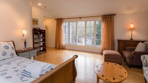 A cozy room with a bed, a wooden table, a sofa, a bookshelf, and a window with curtains. - Edgartown Escape – Walk to Beach & Downtown (Edgartown)