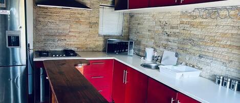 Una cocina moderna con armarios rojos, un refrigerador de acero inoxidable y una encimera de madera.