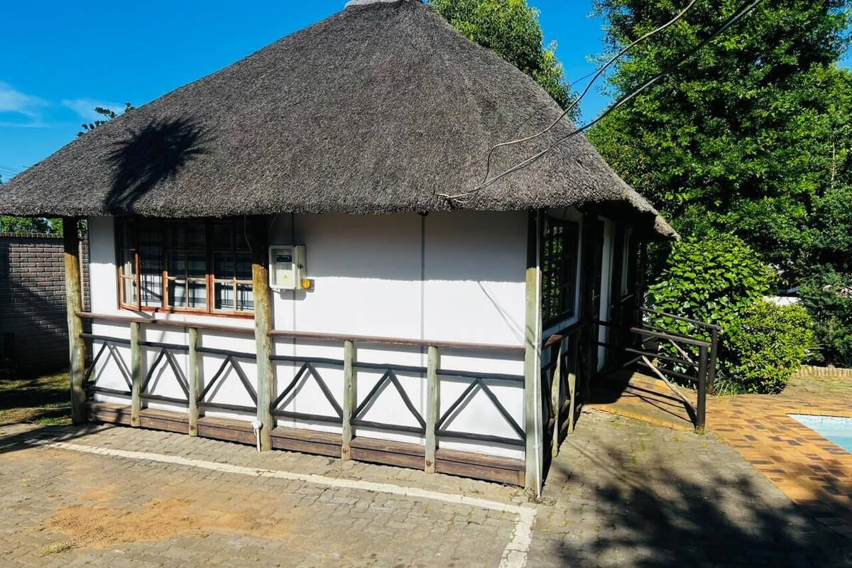 Een gebouw met rieten dak, een witte gevel en houten leuningen, naast een verhard gebied en een zwembad.