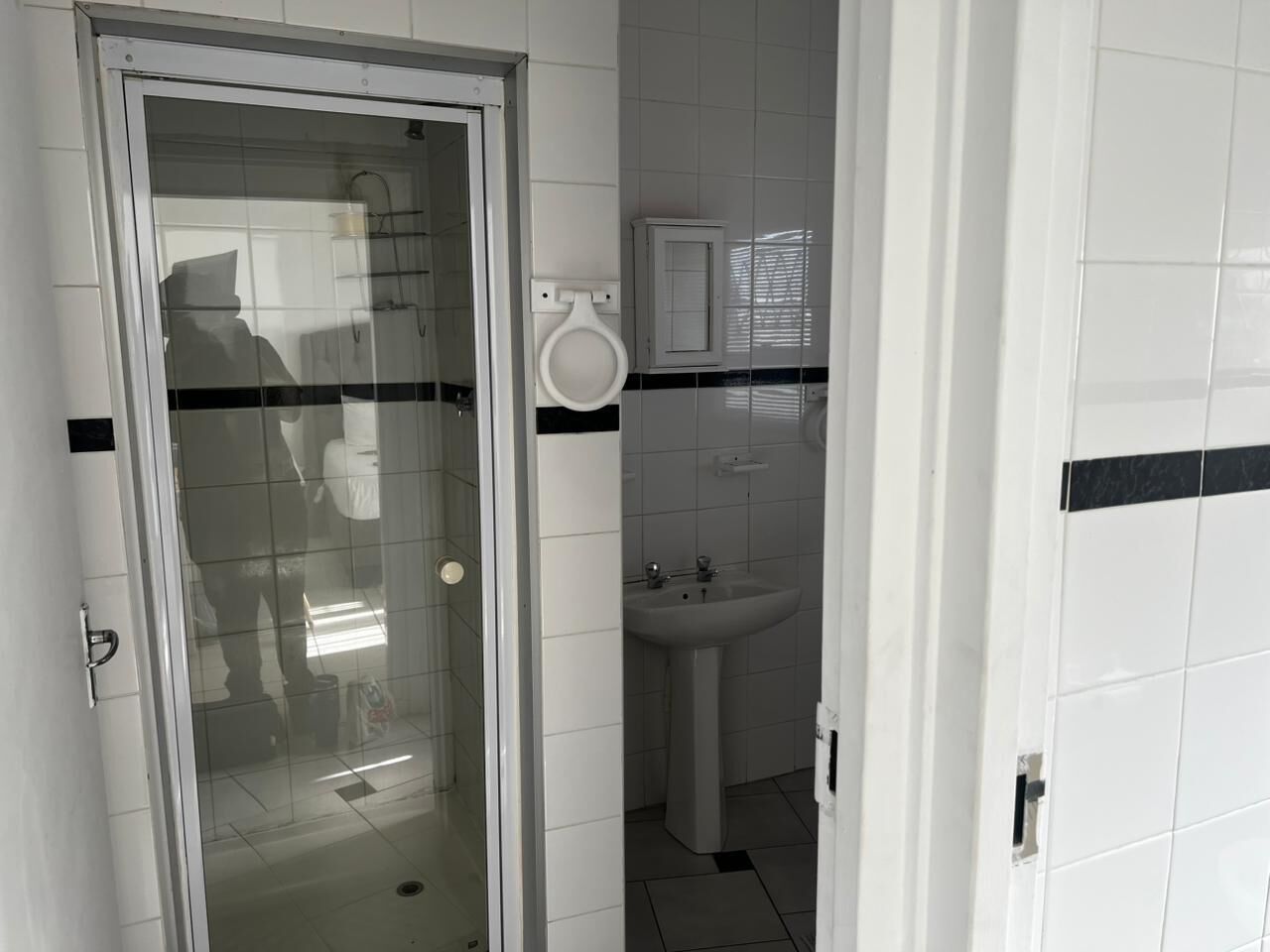 A bathroom with a glass door, a white sink, and a cabinet.