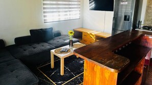 Una sala de estar con sofá, una mesita con un florero, un área de cocina con refrigerador y una barra.