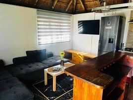Una sala de estar con sofá, una mesita con un florero, un área de cocina con refrigerador y una barra.