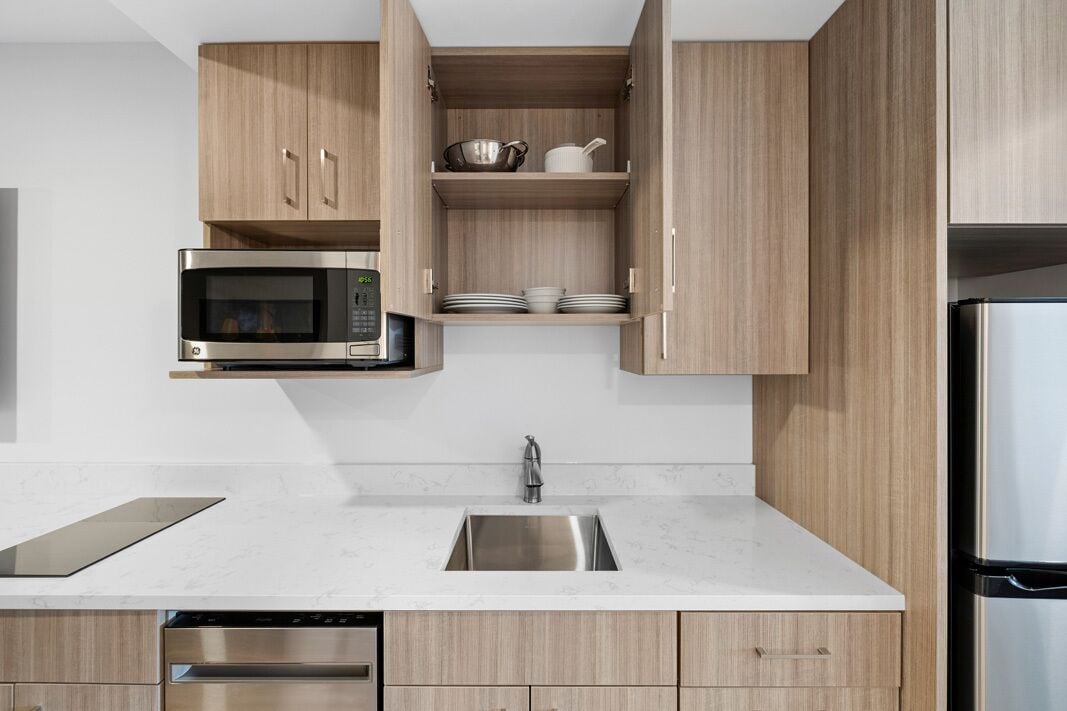 A modern kitchen with wooden cabinets, a stainless steel microwave, a sink, and a built-in oven.
