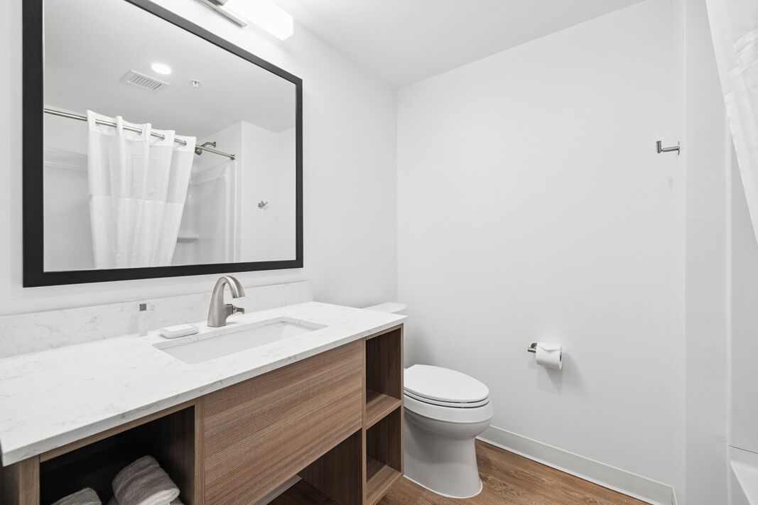 A modern bathroom with a large mirror, a sink, a toilet, and a shower area.