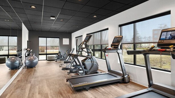 Academia com esteiras, elípticos e bolas de exercício, amplas janelas e design moderno no teto.