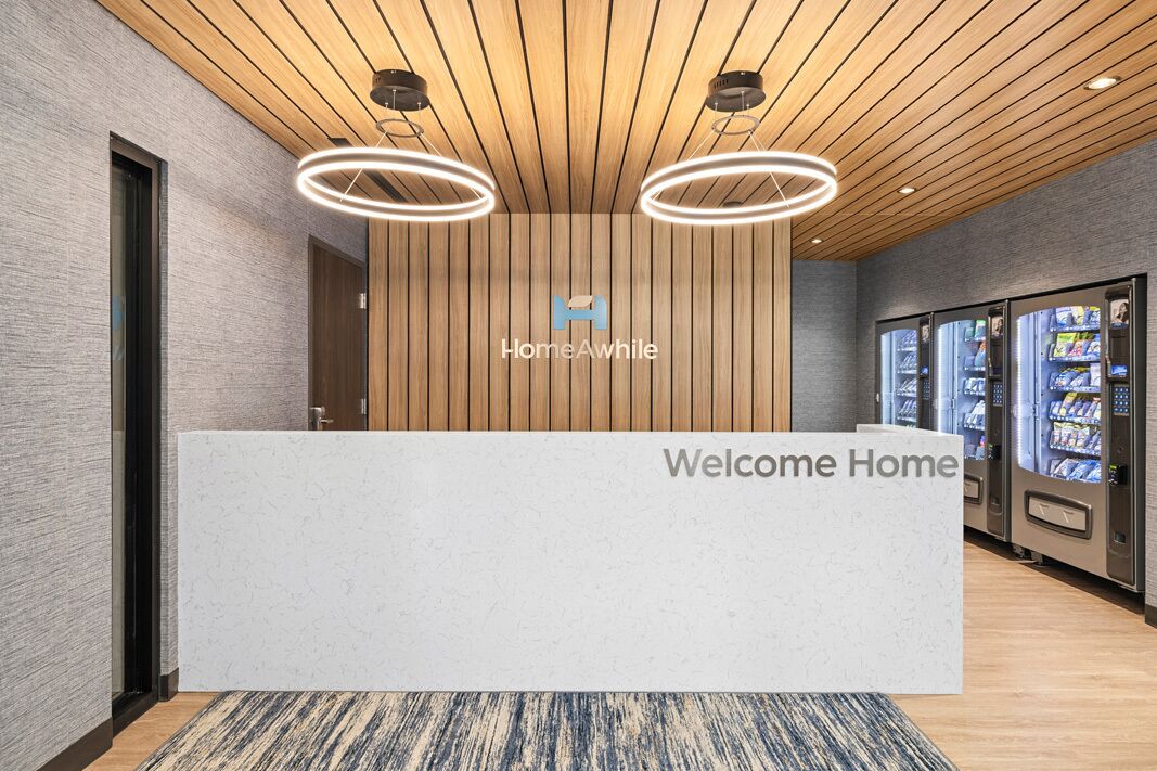 A reception desk with a 'Welcome Home' sign, a logo, and vending machines.