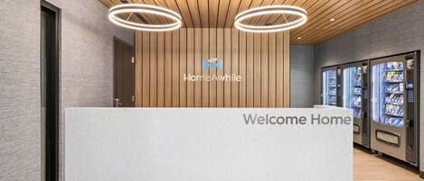 A reception desk with a 'Welcome Home' sign, a logo, and vending machines.