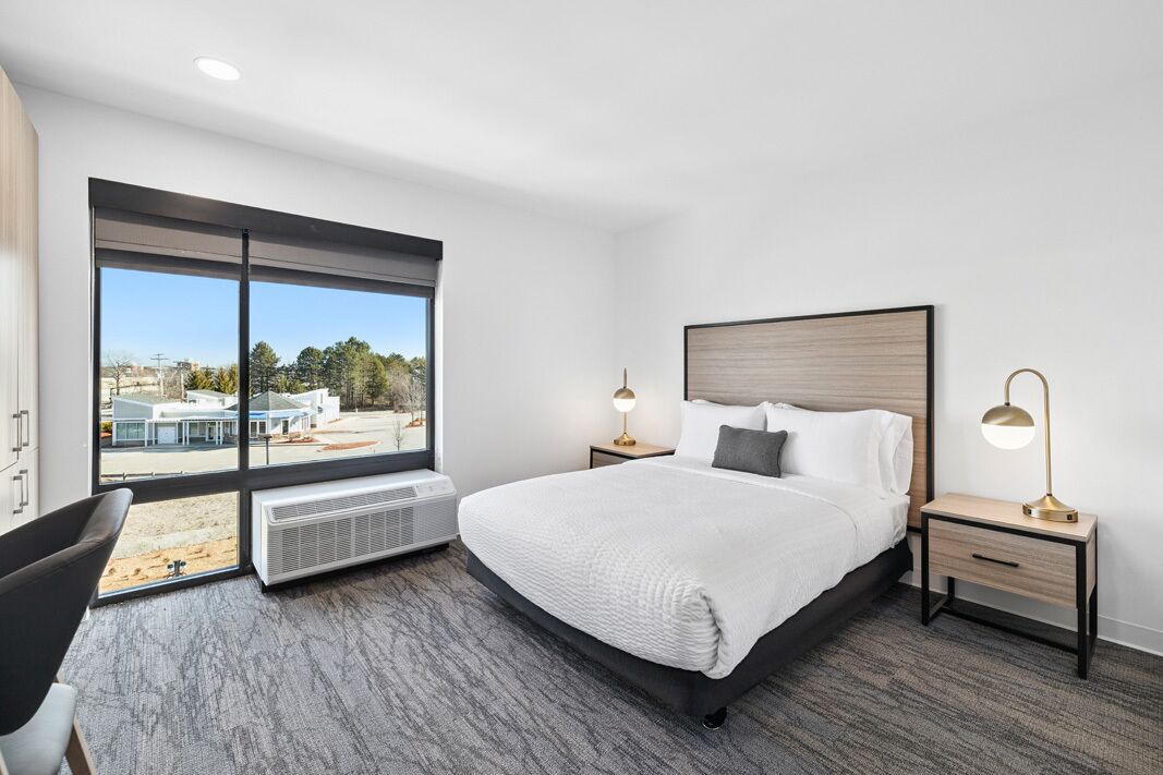 A modern hotel room with a large bed, two bedside tables, a desk, and a chair.