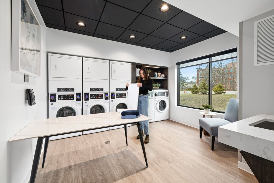 A modern laundry room with multiple washing machines, a table, and a chair.