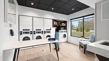 A modern laundry room with multiple washing machines, a table, and a chair.