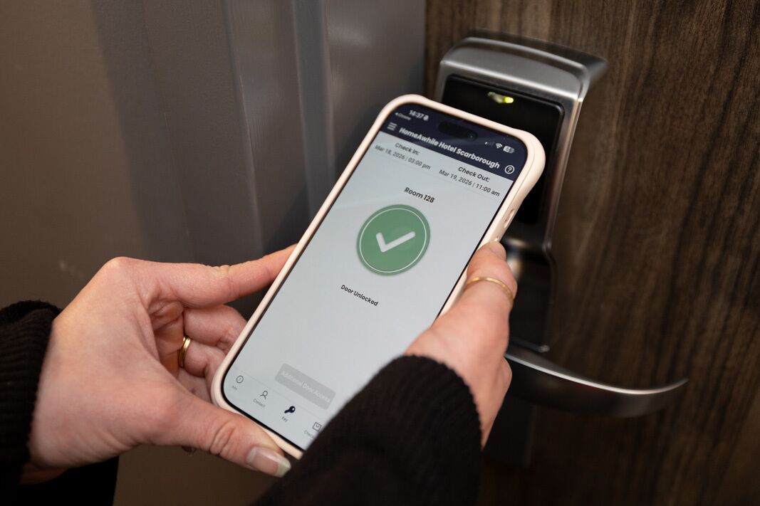 Una persona usa un teléfono inteligente para registrarse en un hotel, con una interfaz digital que muestra detalles de la habitación y la hora de registro.