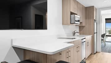 Una cocina moderna con encimera blanca, armarios de madera, microondas integrado y refrigerador de acero inoxidable.