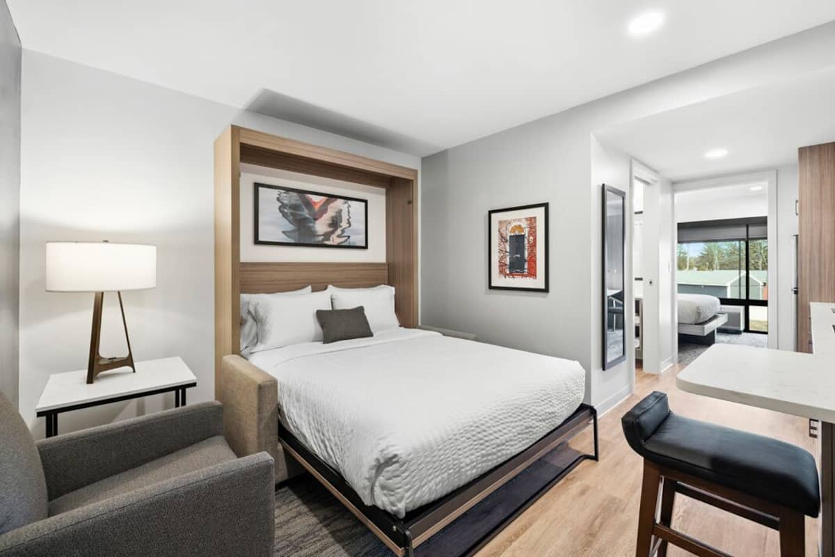 Una habitación de hotel moderna con cama, escritorio, silla, lámpara y obras de arte en las paredes.
