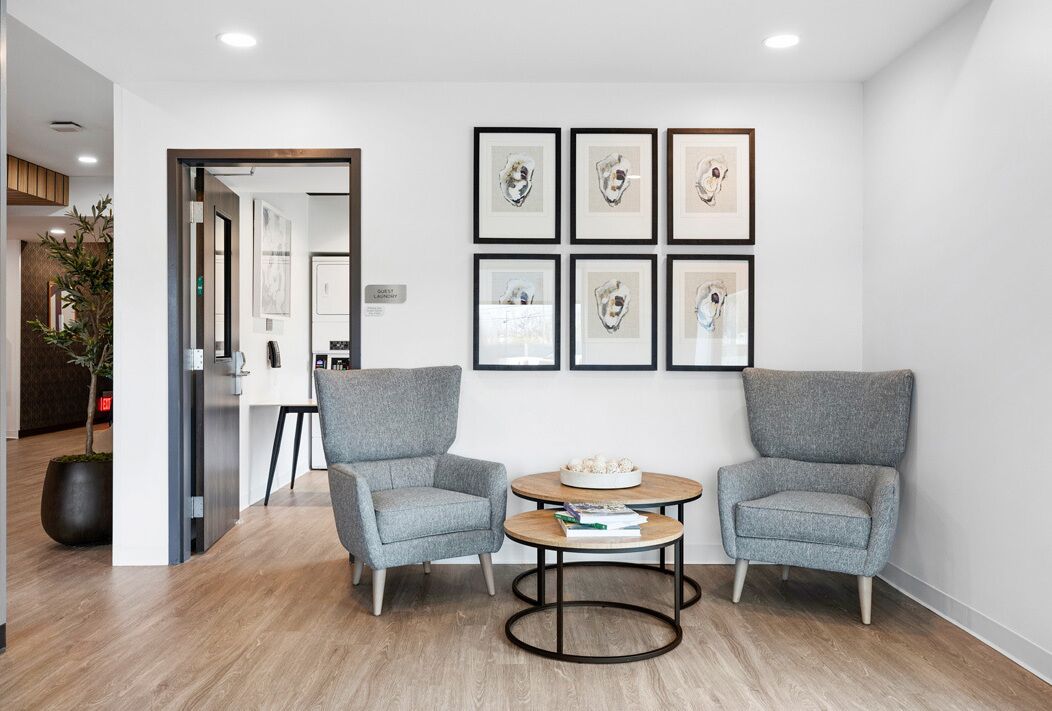 A modern room with two grey armchairs, a round coffee table, and six framed artworks on the wall.