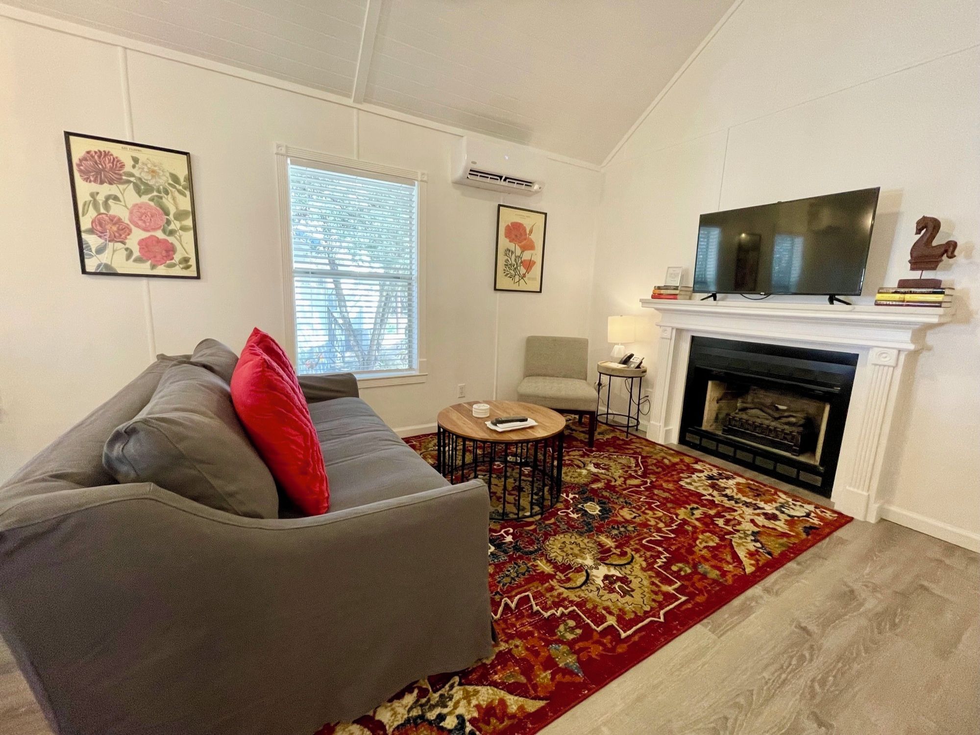 A living room with a grey sofa, a red pillow, a round coffee table, a fireplace, and a mounted TV.