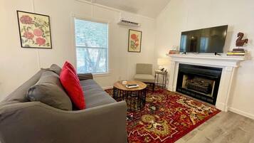 A living room with a grey sofa, a red pillow, a round coffee table, a fireplace, and a mounted TV.