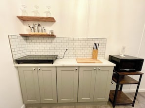 A kitchen with a white tiled backsplash, a wooden shelf above the countertop, and a microwave on a wooden stand. - Cottage 4 Red, Pet-Friendly One-Bedroom Cottage, Private Hot Tub (Wimberley)