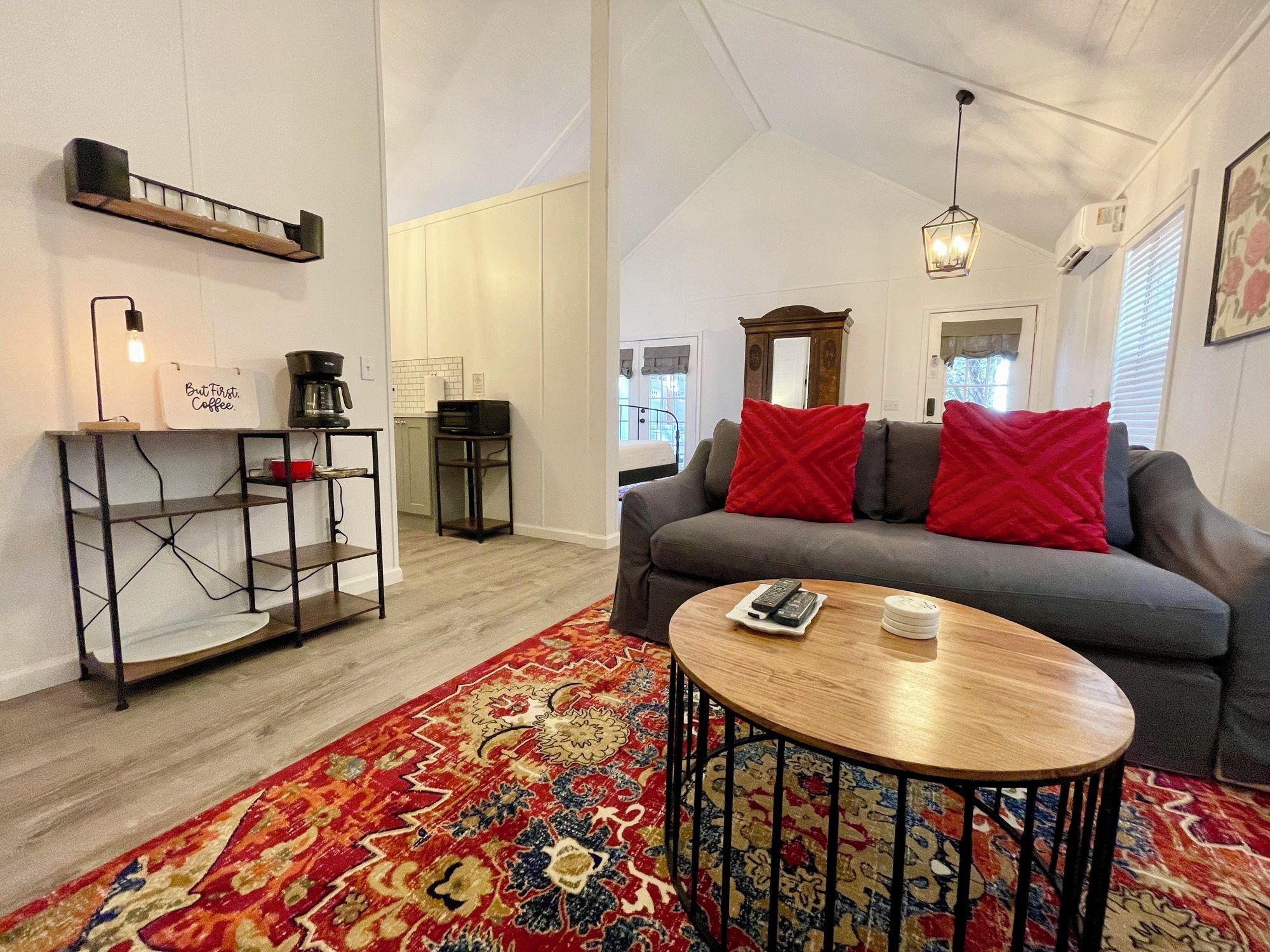 A living room with a sofa, a coffee table, a rug, and a kitchen area with a coffee machine.