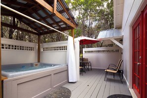 An outdoor hot tub area with a pergola, a covered seating area, and a red door. - Cottage 4 Red, Pet-Friendly One-Bedroom Cottage, Private Hot Tub (Wimberley)