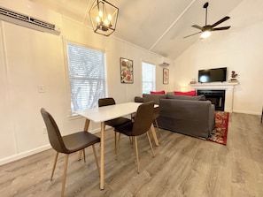 A living room with a dining table, chairs, a sofa, a TV, and a fireplace. - Cottage 4 Red, Pet-Friendly One-Bedroom Cottage, Private Hot Tub (Wimberley)