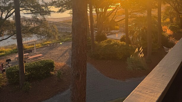 Une vue sur le coucher de soleil depuis une promenade couverte, agrémentée de bancs et d’arbres.