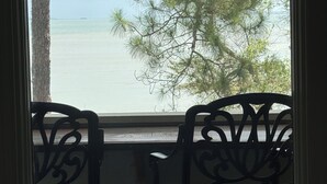 Une vue depuis une fenêtre, avec une table et des chaises, donnant sur une étendue d’eau et des arbres.