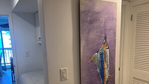 Une chambre à coucher avec un lit, un tableau représentant un poisson accroché au mur et une porte avec une fenêtre.