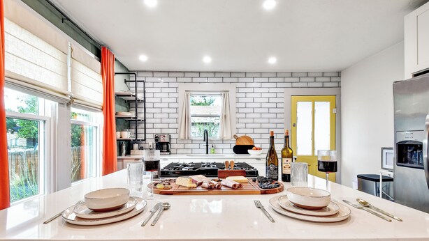 Una cocina moderna con una isla central, salpicadero de ladrillo blanco y una puerta amarilla.